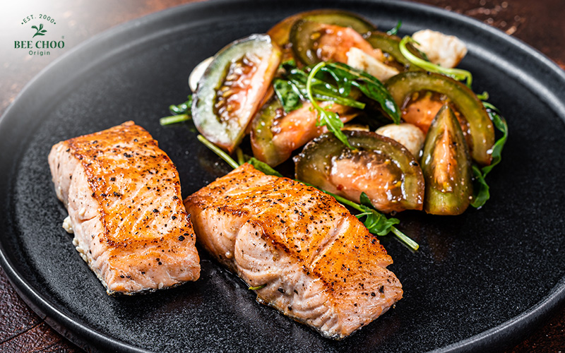 A plate of roasted salmon with tomatoes and herbs.