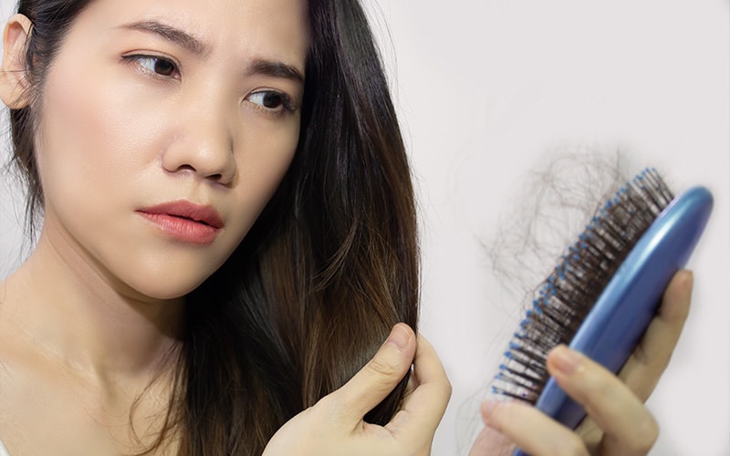 asian-woman-looking-worried-at-loose-strands-caught-on-a-hairbrush